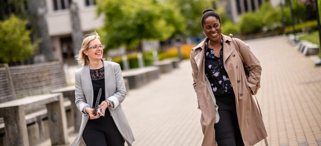 One black and one white woman walking together on a path, laughing. 
